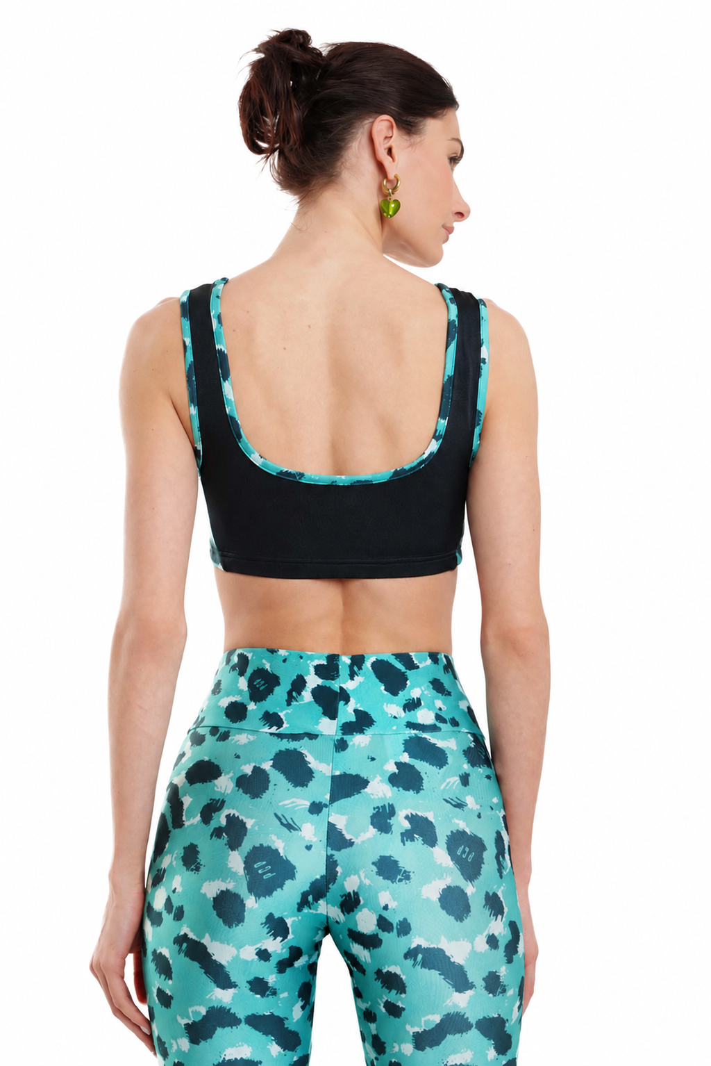 A woman shown from the back wearing a black sports bra with turquoise and white patterned trim, paired with matching high-waisted leggings featuring a turquoise, black, and white abstract pattern, against a plain white background.
