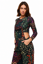 A woman modeling a long-sleeve black maxi dress with a vibrant multicolor celestial and floral print, featuring side cutouts, against a plain white background.