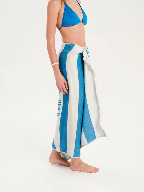 Person wearing a blue bikini top and white and blue striped sarong on a white background