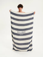 Man holding a large striped towel with 'Sun of a Beach' branding on a white background