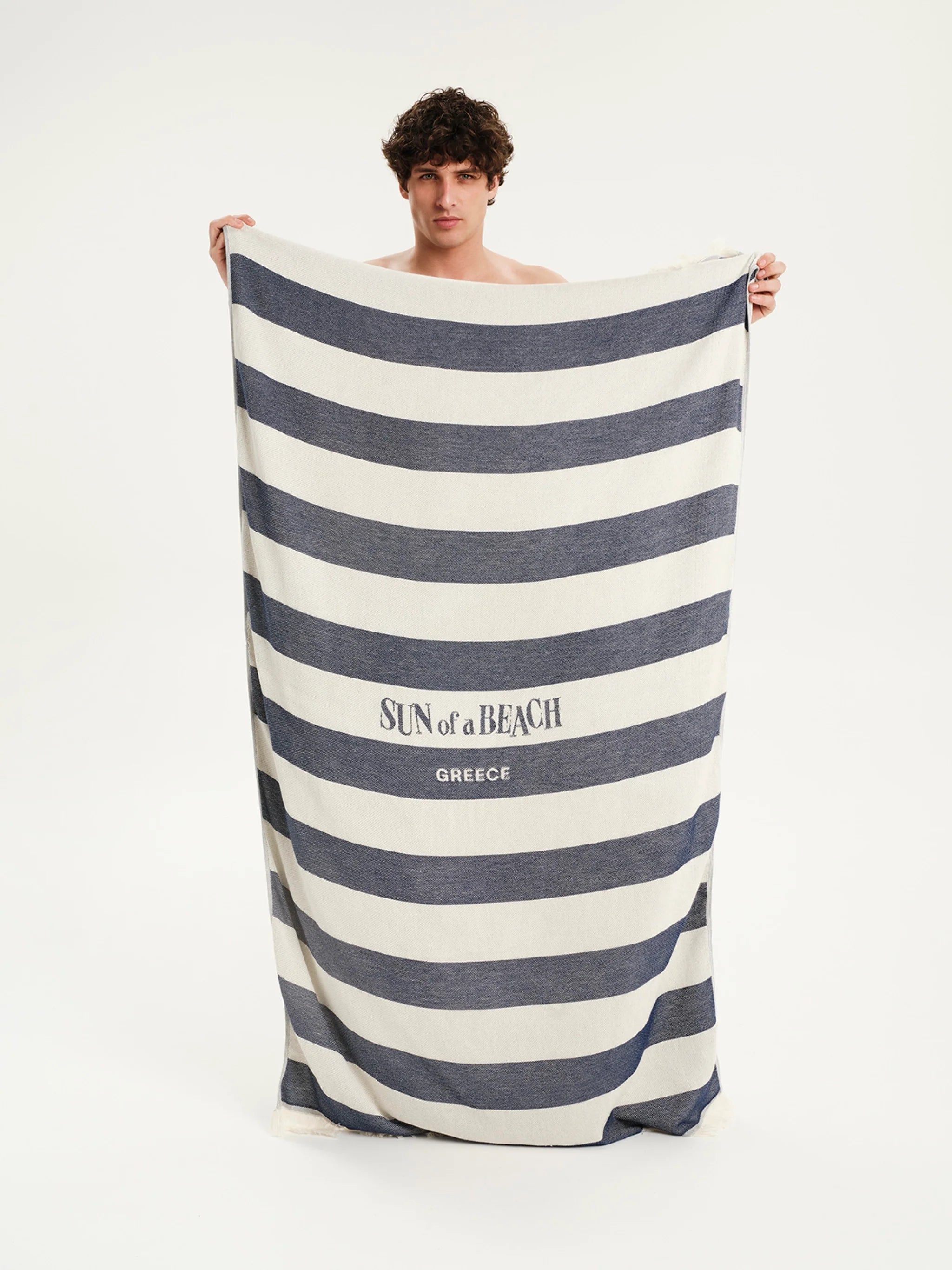 Man holding a large striped towel with 'Sun of a Beach' branding on a white background