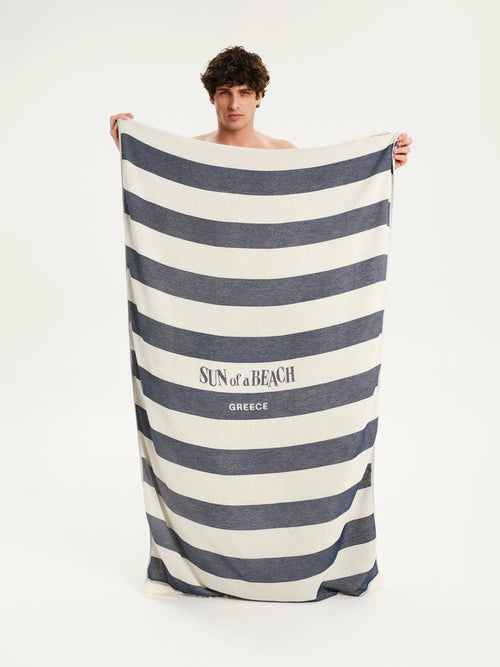 Man holding a large striped towel with 'Sun of a Beach' branding on a white background