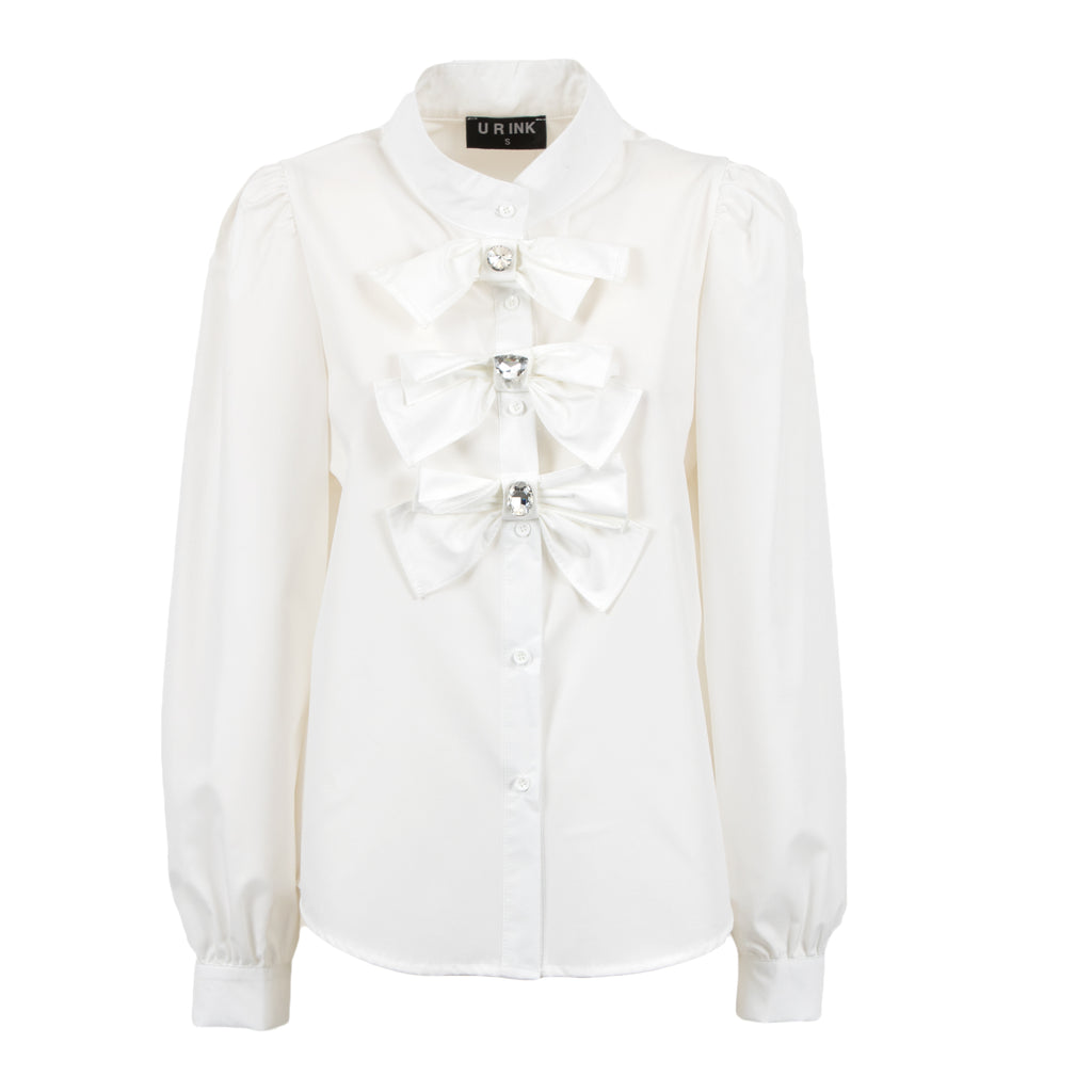 An off-white long-sleeve blouse with a high collar, buttoned front, and three large decorative bow details on the chest, each accented with a small rhinestone. The brand label on the collar reads 'L'EAU D'INCH'.
