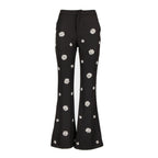 Black flared pants with white embroidered daisy patterns, shown against a plain white background.