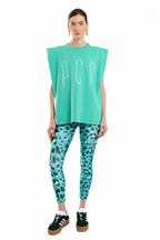 A model stands against a white background wearing a sleeveless mint green top with rhinestone lettering, matching patterned leggings, and black sneakers.