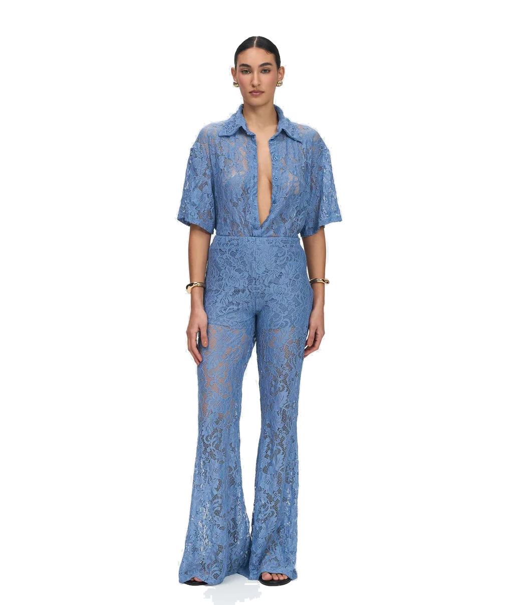 A model stands against a plain white background wearing a light blue lace short-sleeve jumpsuit with a deep plunging neckline and wide-leg pants.