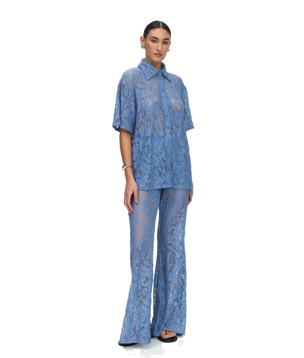 A model stands against a white studio background wearing a matching blue lace two-piece outfit consisting of a short-sleeve collared button-front top and wide-leg pants.