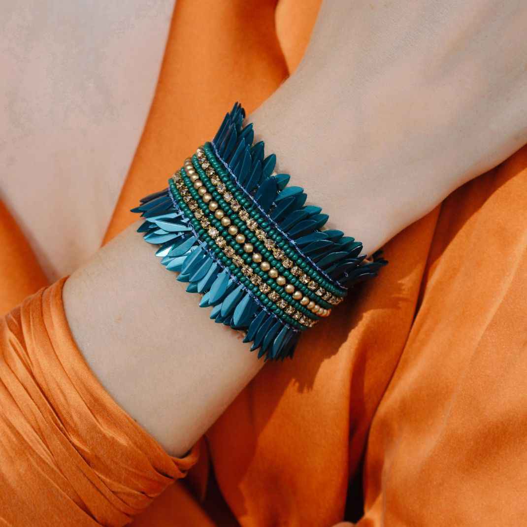 Close-up of a wrist wearing a blue beaded bracelet against an orange fabric background