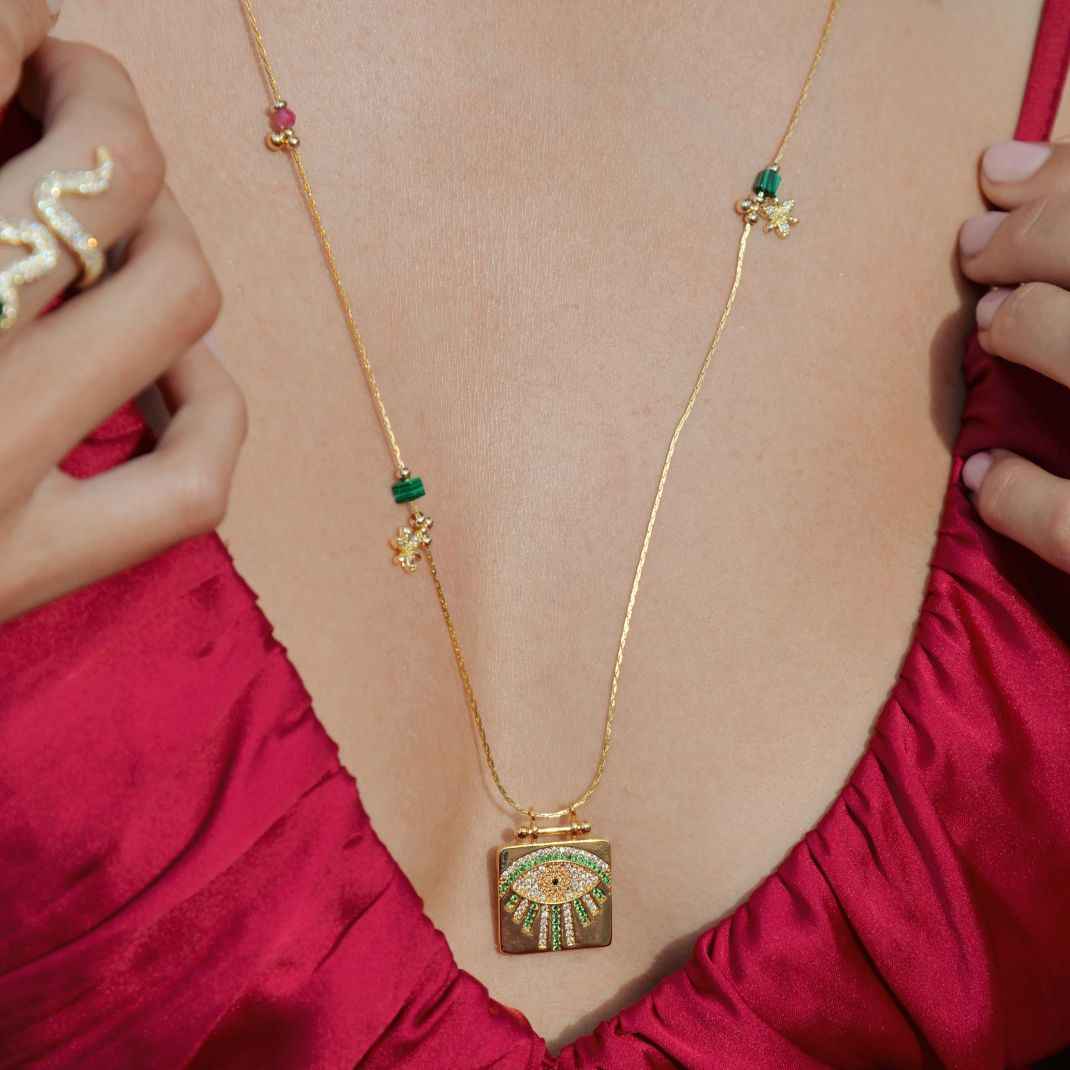 Gold necklace with green gemstones worn by a person in a red garment