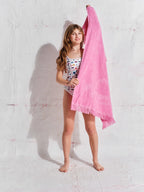 Young girl holding a pink towel against a white wall