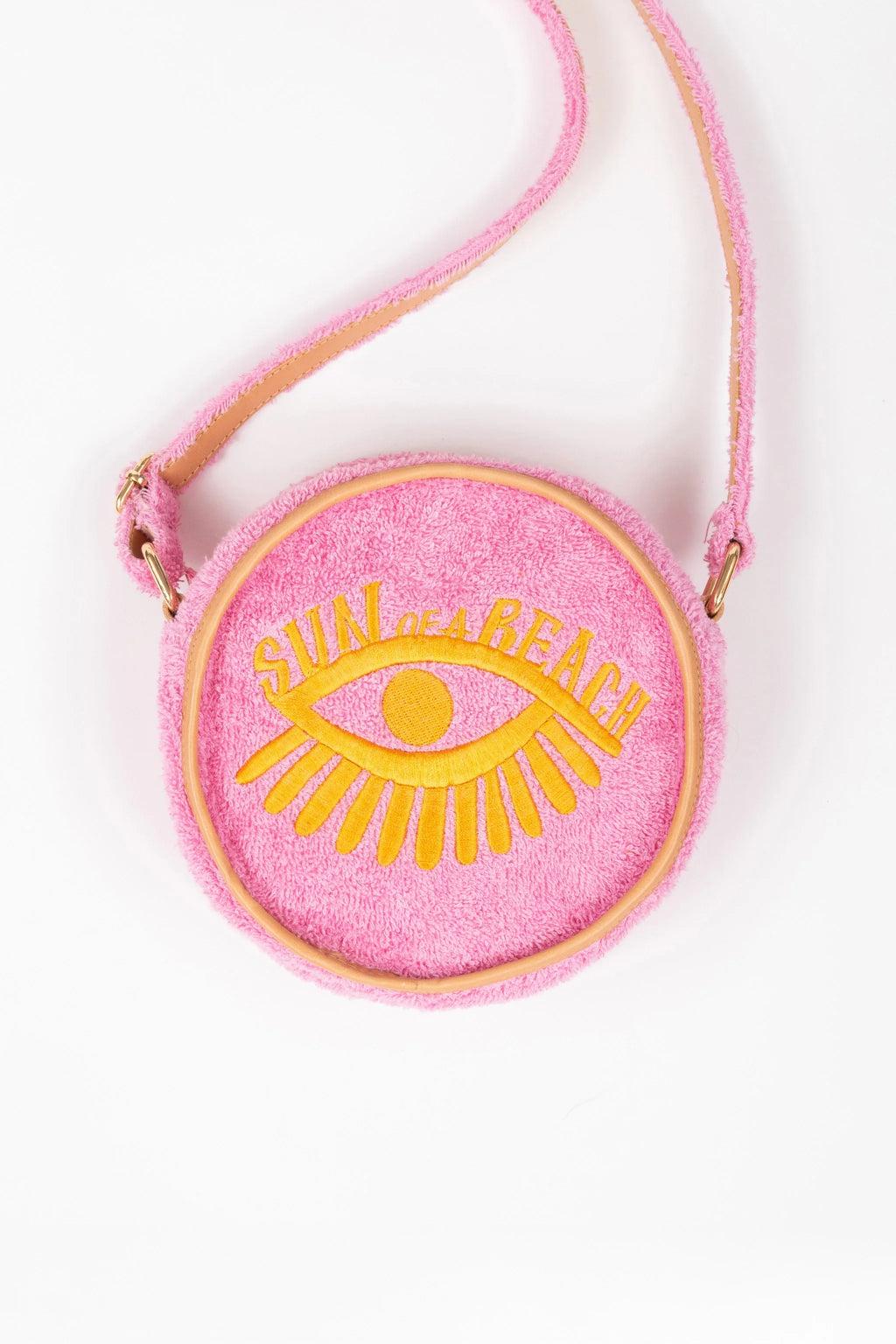 A pink fuzzy round crossbody bag with a yellow embroidered eye and the text 'SUN OF A BEACH' on the front, shown on a plain white background.