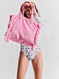 Person wearing a pink hooded towel and a patterned swimsuit against a plain background