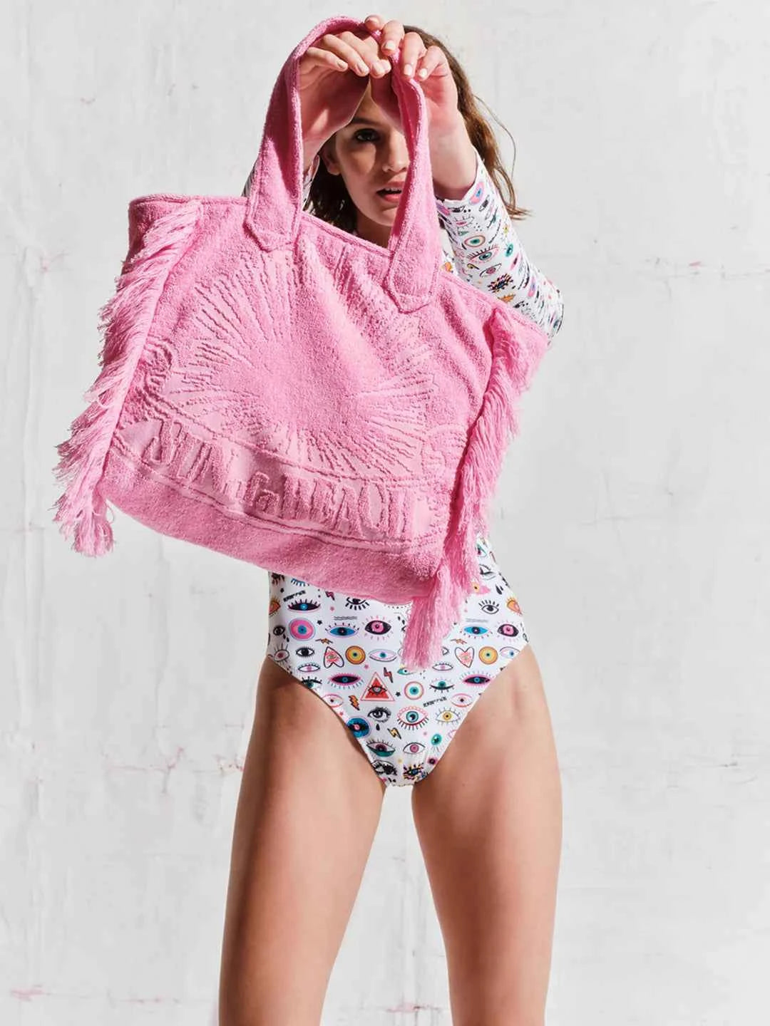Person wearing a pink hooded towel and a patterned swimsuit against a plain background