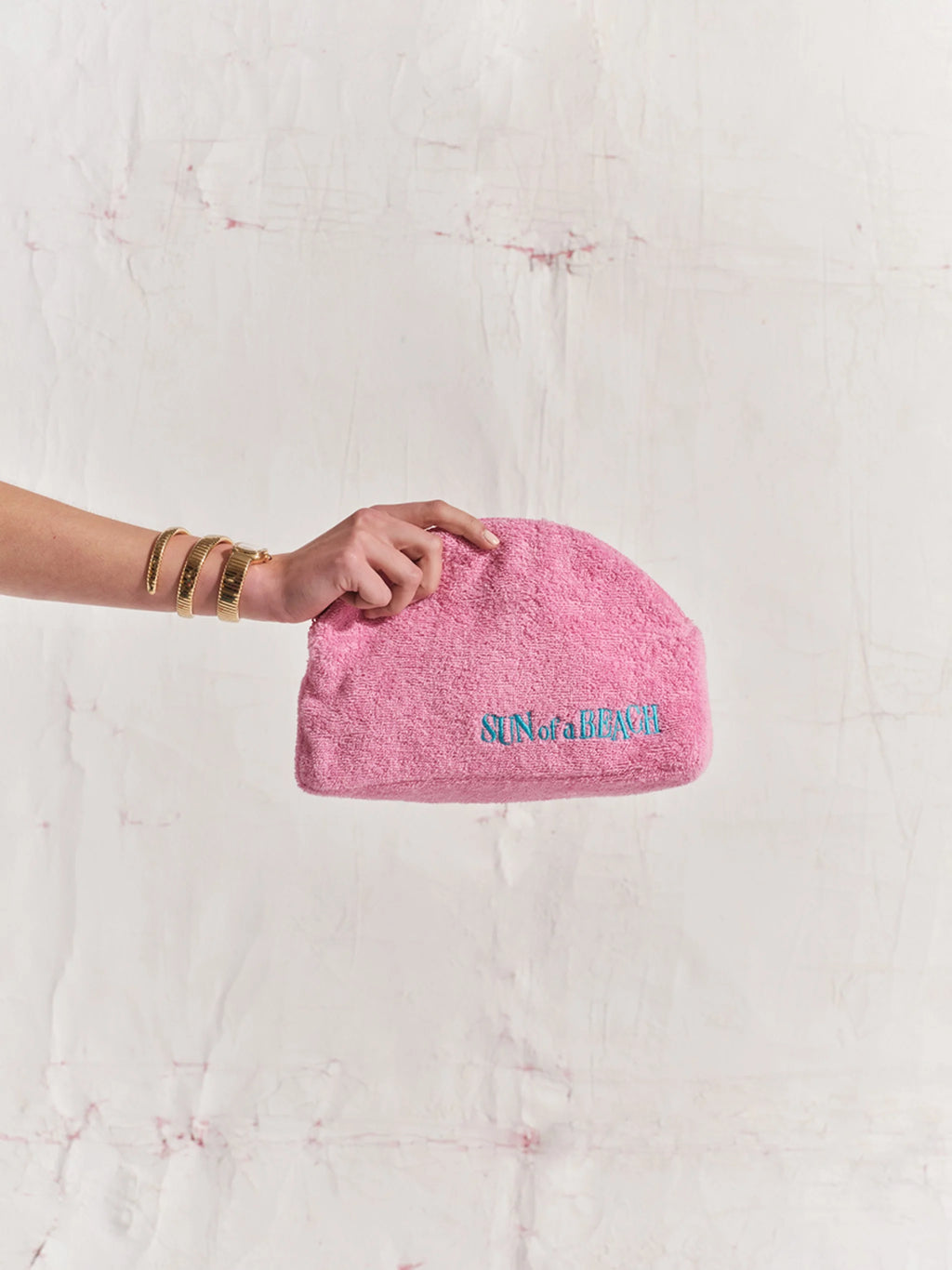 Pink pouch with text held by a hand against a textured white background