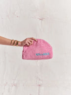 Pink pouch with text held by a hand against a textured white background