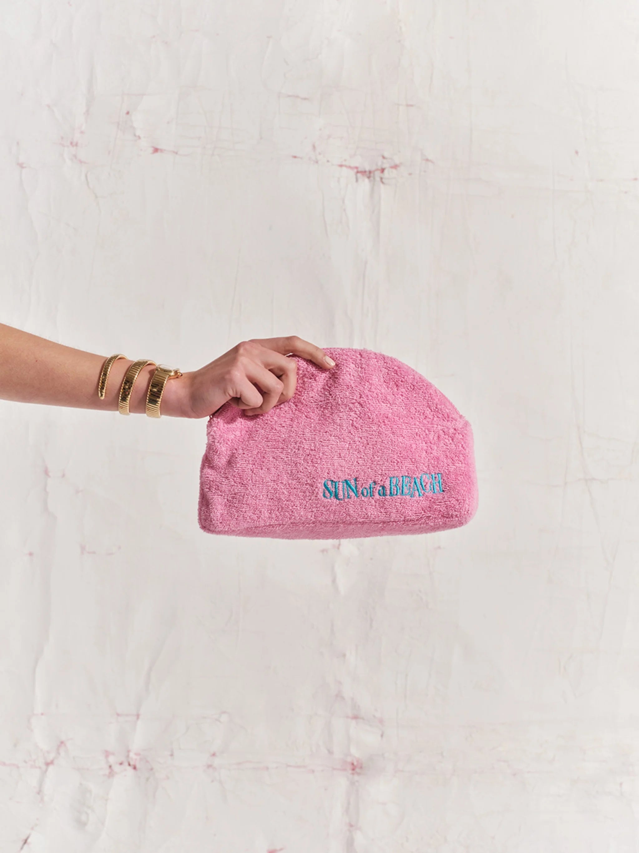 Pink pouch with text held by a hand against a textured white background