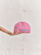 Pink textured pouch held by a hand on a light pink background