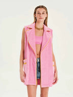 Woman wearing a pink vest over a pink top and denim shorts on a white background