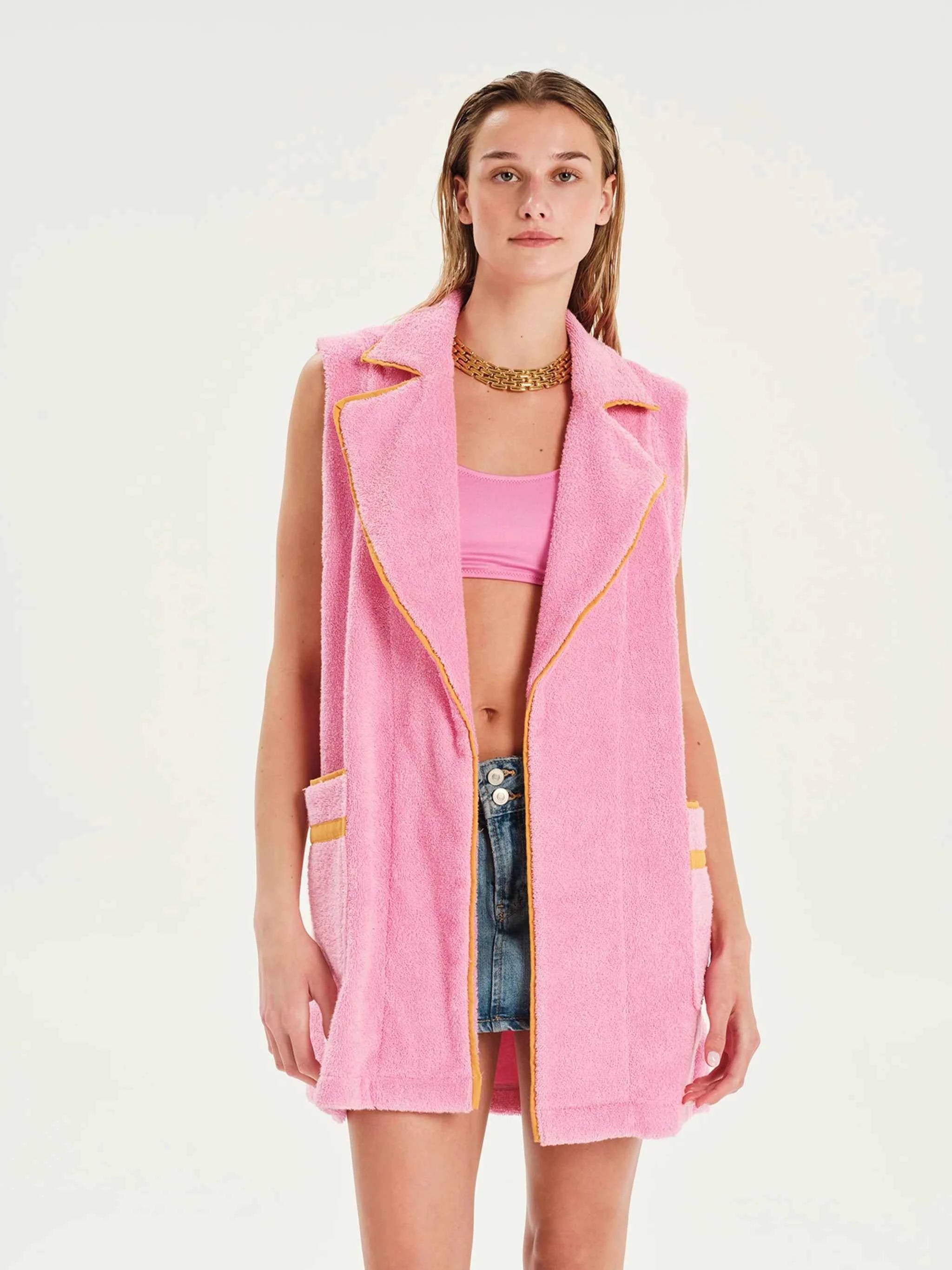 Woman wearing a pink vest over a pink top and denim shorts on a white background