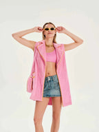 Woman wearing a pink jacket, pink top, and denim shorts on a white background