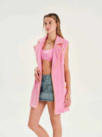 Woman wearing a pink vest over a pink top and denim skirt on a white background