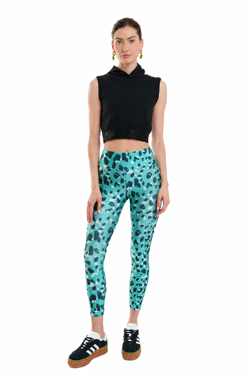 Woman wearing a black sleeveless top and teal leggings with a pattern on a white background