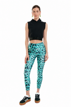 Woman wearing a black sleeveless top and teal leggings with a pattern on a white background