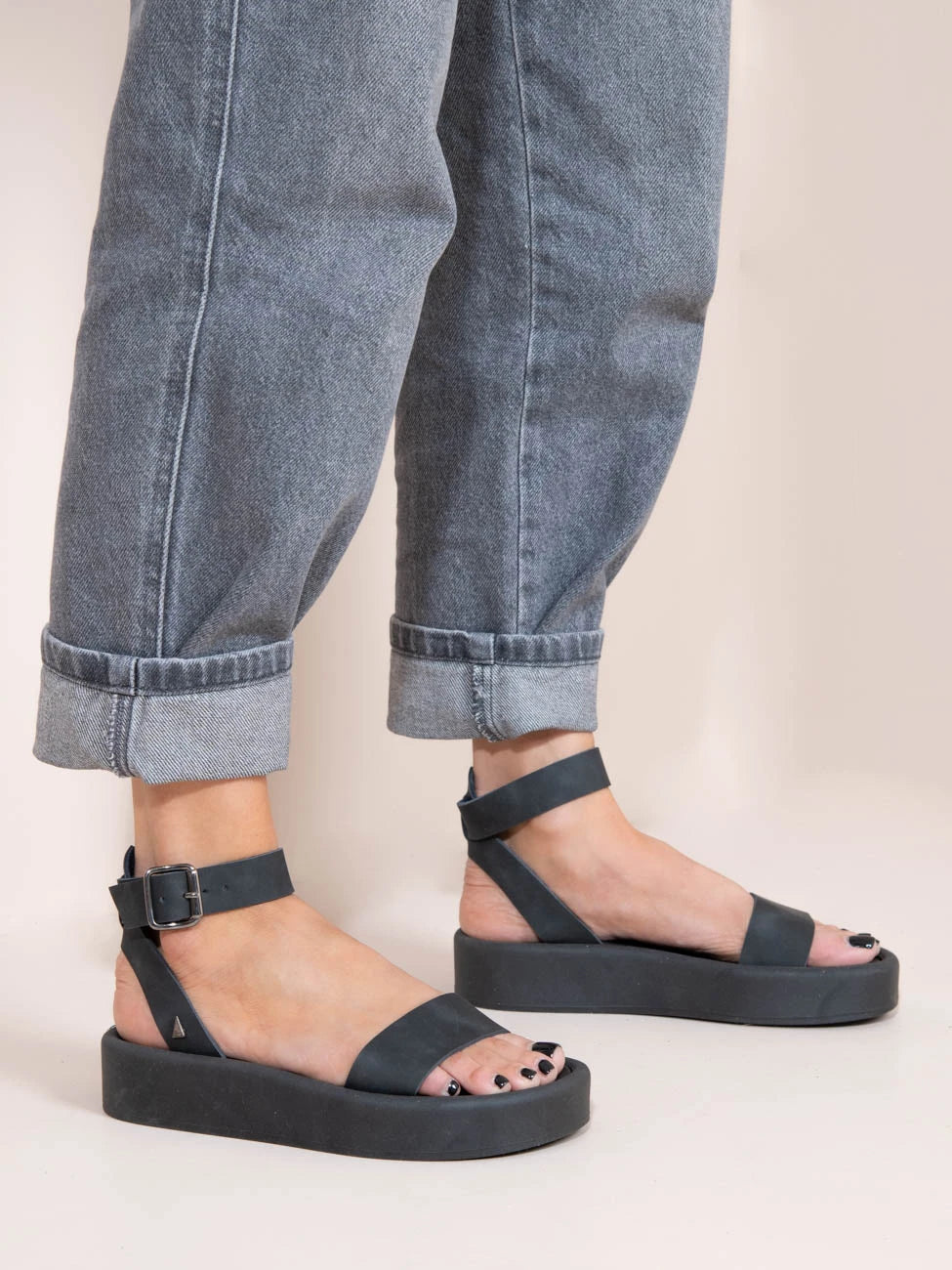 Black sandals worn with rolled-up jeans on a light background