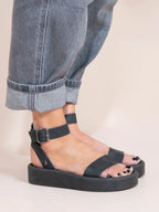 Black sandals worn with rolled-up jeans on a neutral background