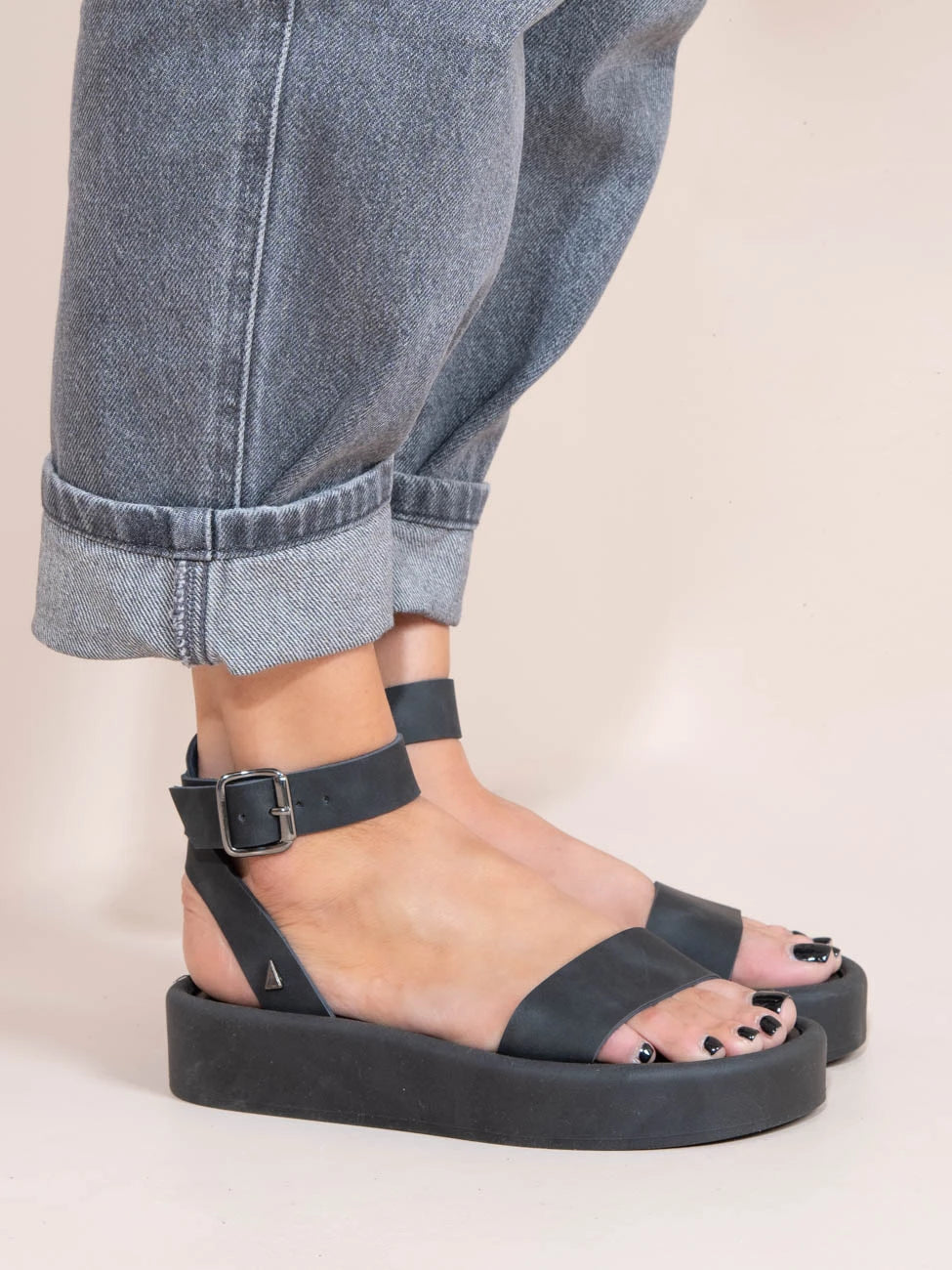 Black sandals worn with rolled-up jeans on a neutral background