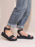 Black sandals worn with rolled-up jeans on a neutral background