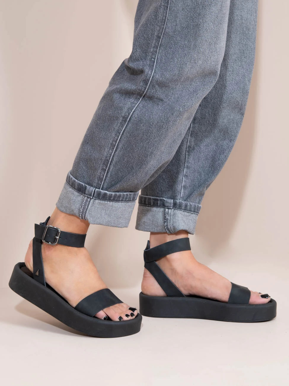 Black sandals worn with rolled-up jeans on a neutral background