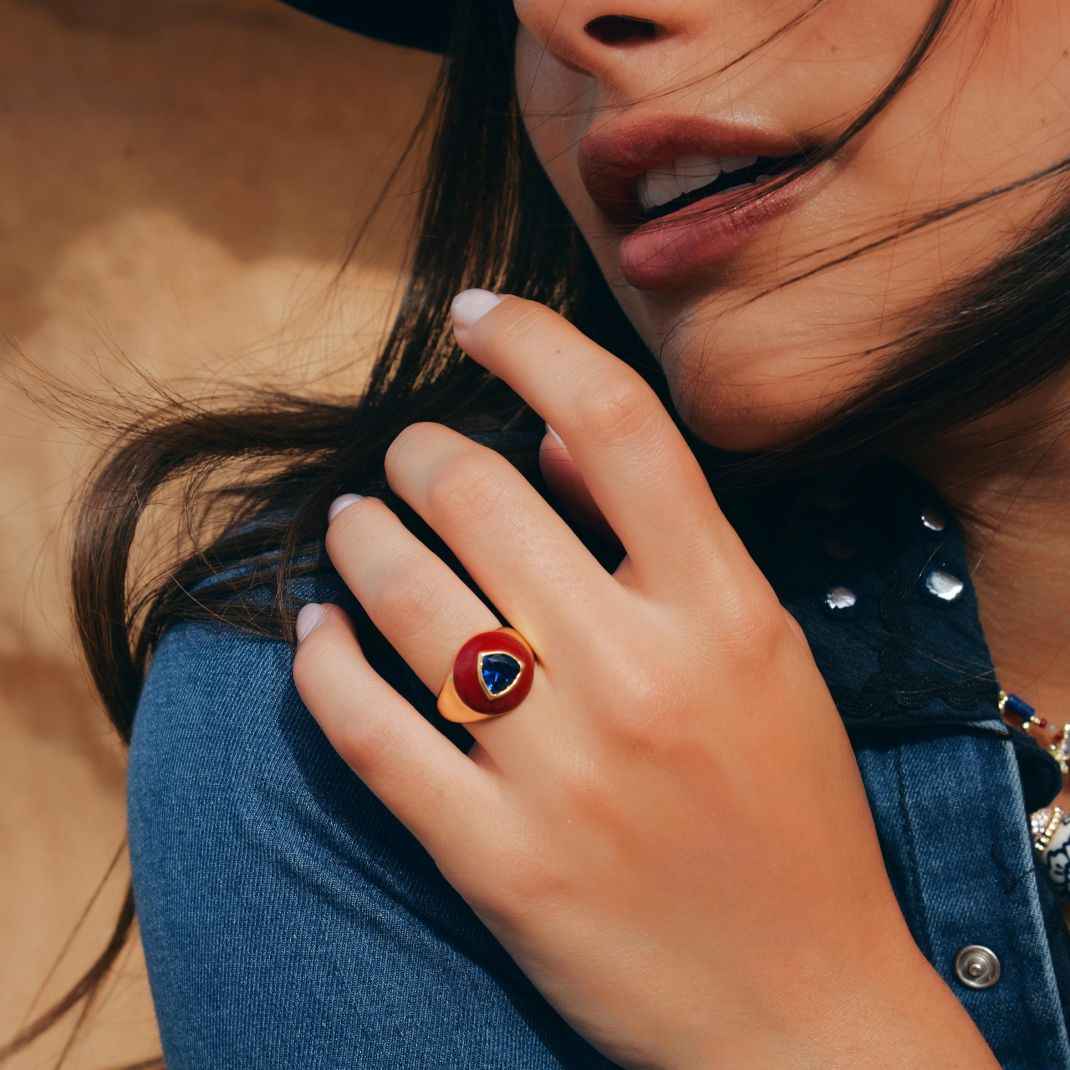 Close-up of a hand wearing a ring with a blue stone, against a blurred background.