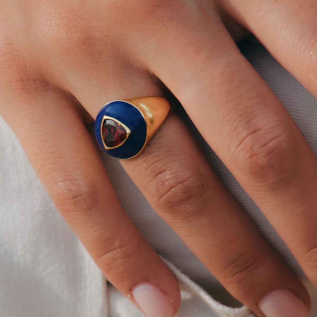 Close-up of a hand wearing a ring with a blue stone on a neutral background