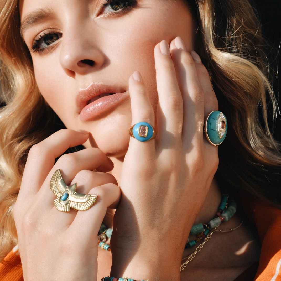 Close-up of a woman's hands wearing multiple turquoise rings with gold accents.