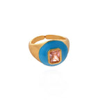 Gold ring with a blue bezel and pink gemstone on a white background