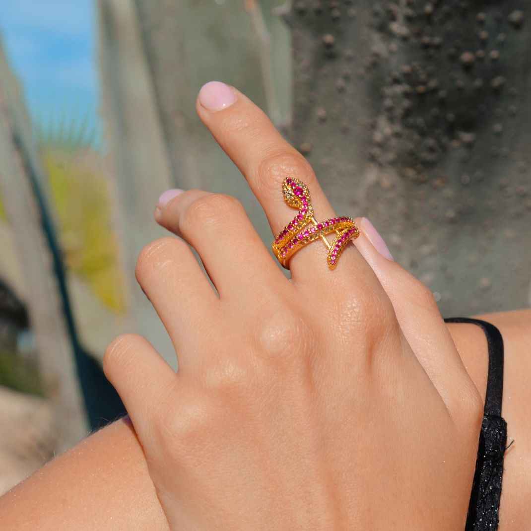 Hand wearing a gold ring with red gemstones against a blurred outdoor background