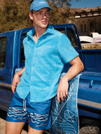 Man wearing a blue shirt and shorts leaning against a blue truck.