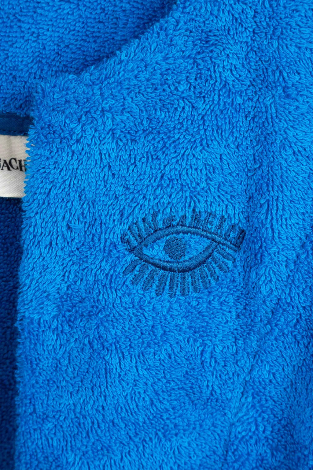 Close-up of a blue textured fabric with an embroidered eye design, featuring the brand 'Coach'.