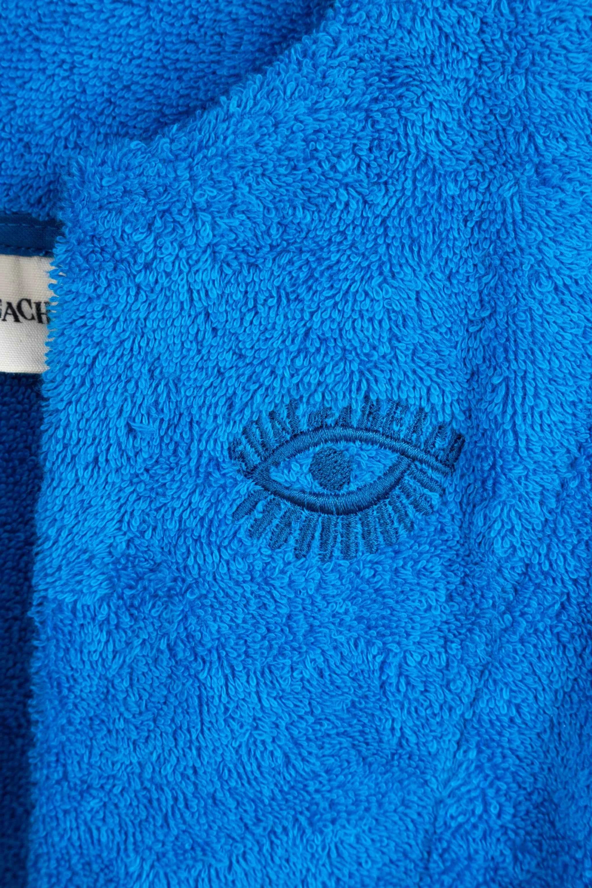 Close-up of a blue textured fabric with an embroidered eye design, featuring the brand 'Coach'.