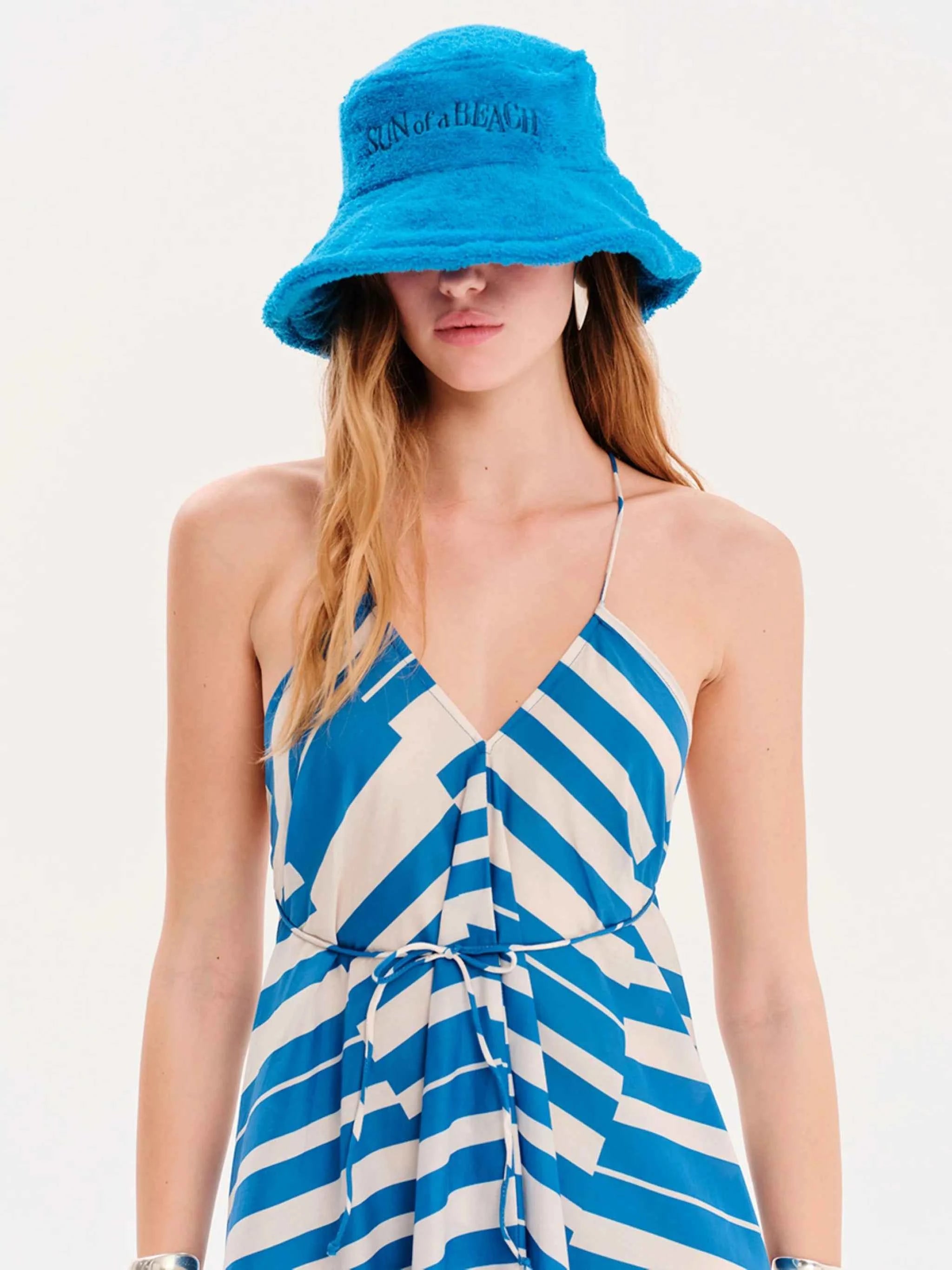 Woman wearing a blue and white striped dress with a matching bucket hat on a light gray background