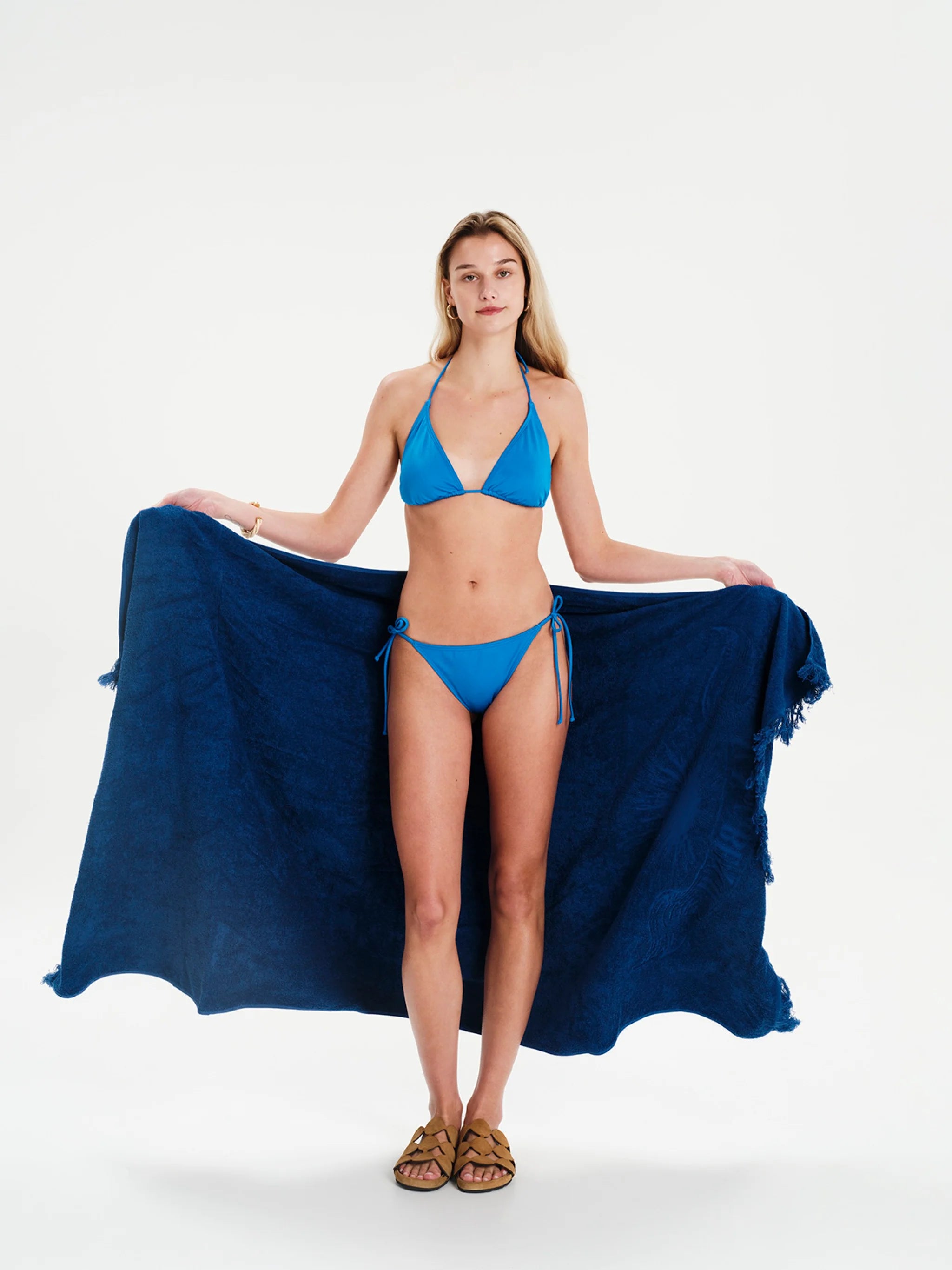Woman wearing a blue bikini holding a matching blue towel on a white background