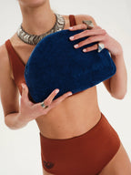 Person holding a blue clutch against a neutral background