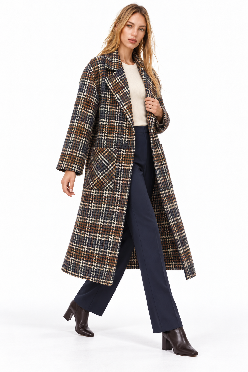 A woman modeling a long brown and beige plaid coat over a cream top, navy wide-leg pants, and dark brown ankle boots, photographed against a plain white studio background.
