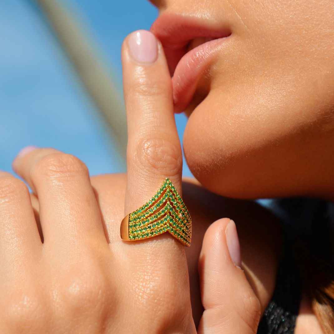 Close-up of a hand wearing a green and gold chevron-patterned ring against a blurred background.