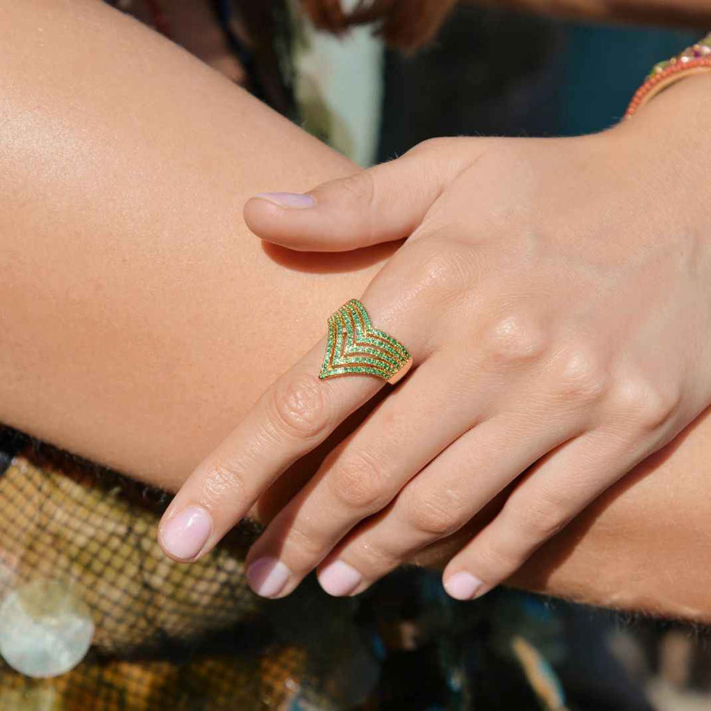 Close-up of a hand wearing a green and gold ring with a blurred background