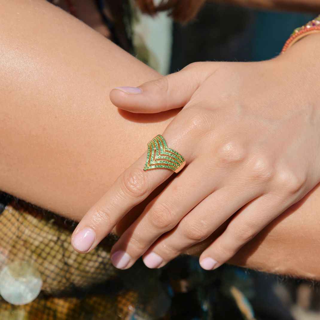 Close-up of a hand wearing a green and gold ring with a blurred background
