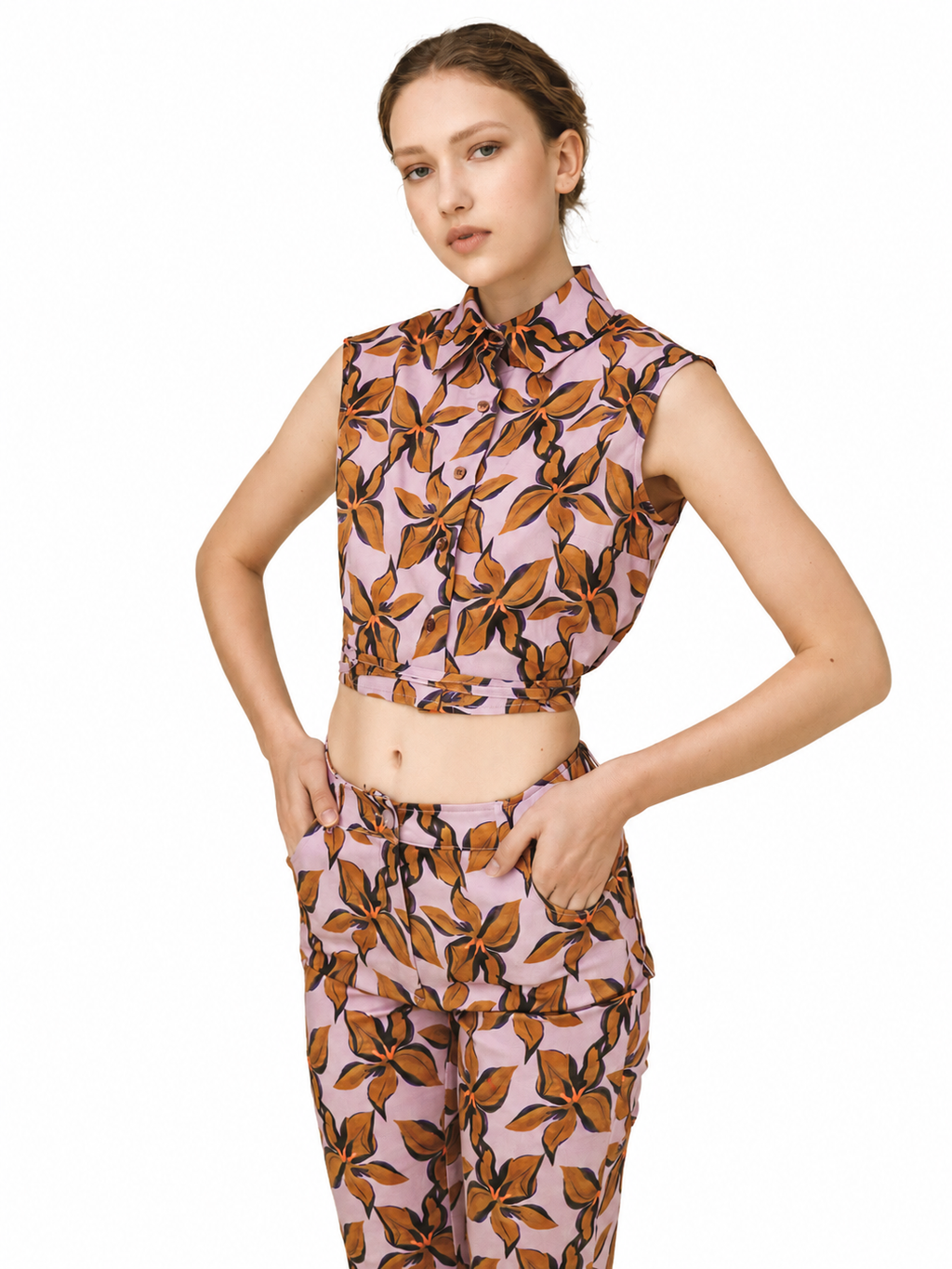 A model wearing a matching sleeveless collared top and trousers set in a dusty pink fabric with a brown and black leaf pattern, shot against a solid white background.