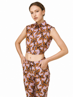 A model wearing a matching sleeveless collared top and trousers set in a dusty pink fabric with a brown and black leaf pattern, shot against a solid white background.