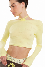A woman wearing a pale yellow long-sleeve crop top with a subtle allover tonal pattern and a crisscross neckline, paired with patterned shorts against a plain white background.